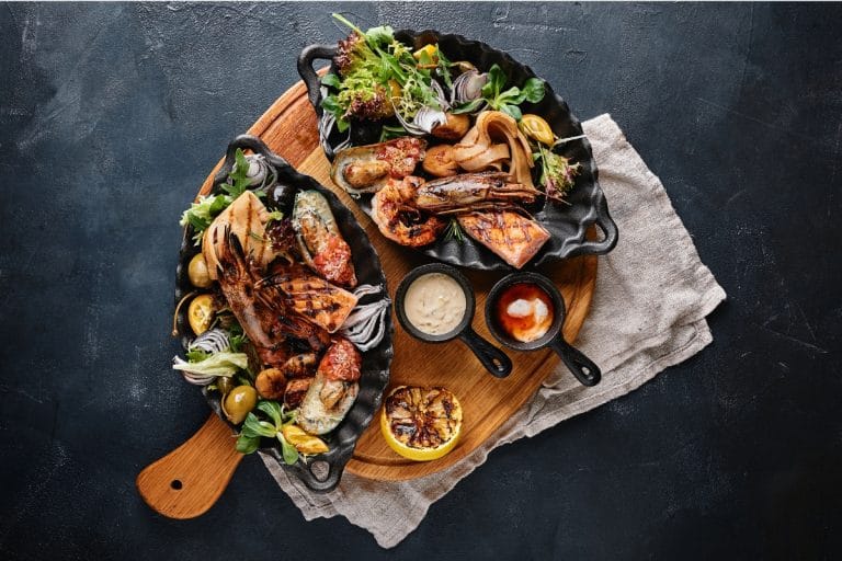Mariscada gallega servida en platos de hierro con mariscos variados como langostinos, mejillones, pulpo y salmón, acompañada de salsas y verduras frescas, típica de Santiago de Compostela.