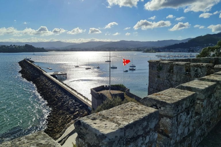 Vista desde las murallas del Parador de Baiona, con el puerto deportivo, barcos y el espigón al atardecer sobre la ría gallega