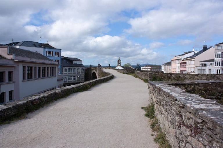 Paseo sobre la antigua Muralla Romana de Lugo, Patrimonio de la Humanidad, con vistas a los edificios de la ciudad y un campanario