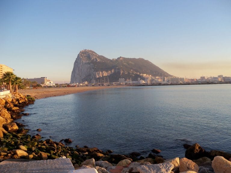 Vista de la playa de Algeciras con la desembocadura al mar y el peñón de Gibraltar al fondo bajo un cielo despejado.