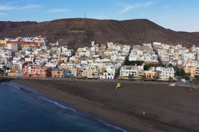 Vista aérea de la playa de Gran Tarajal con arena oscura y edificios coloridos al fondo en Fuerteventura.