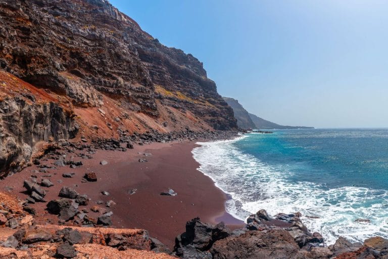 Vista de la Playa de El Verodal con arena volcánica rojiza, acantilados escarpados y aguas cristalinas del Atlántico.