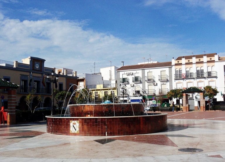 Fuente central en la Plaza de España de Gibraleón, Huelva, rodeada de edificios tradicionales y ambiente urbano