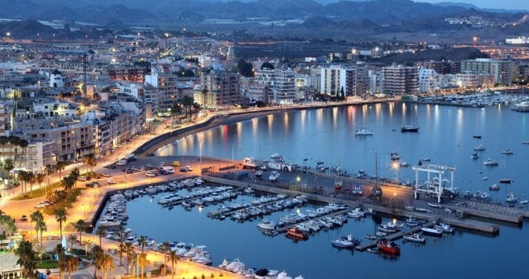 Vista panorámica del puerto de Águilas (Murcia) al atardecer con barcos amarrados y luces de la ciudad reflejadas en el agua