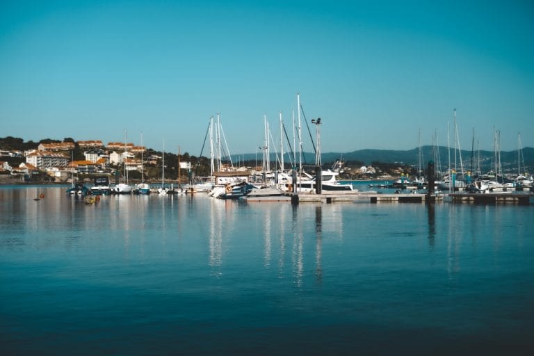 El concurrido puerto deportivo de Sanxenxo, Pontevedra, Galicia, con numerosos yates y veleros atracados y el pueblo costero extendiéndose a lo largo de la ría.