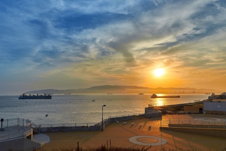 Atardecer en Algeciras sobre el estrecho con el sol reflejado en el agua y varios barcos en el horizonte.