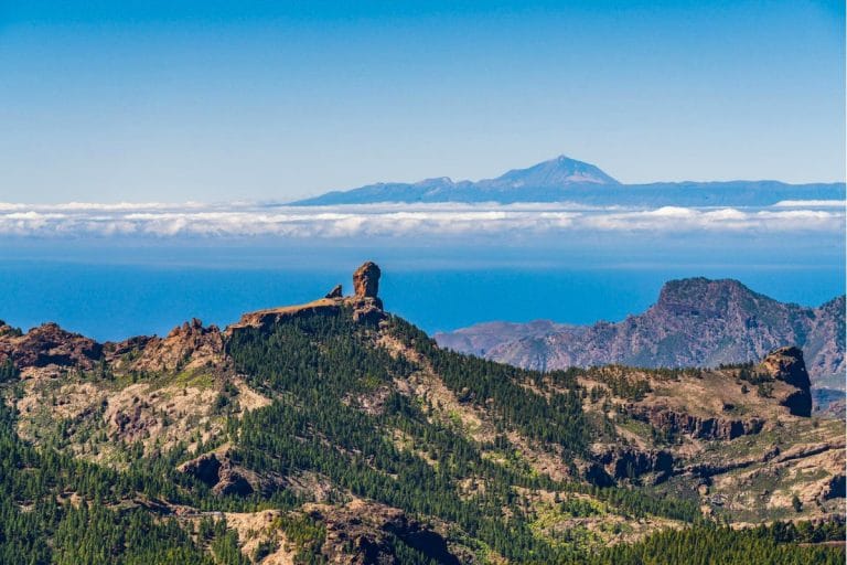 Panorámica del Roque Nublo en Gran Canaria con el Teide al fondo y cielo despejado sobre el mar de nubes.