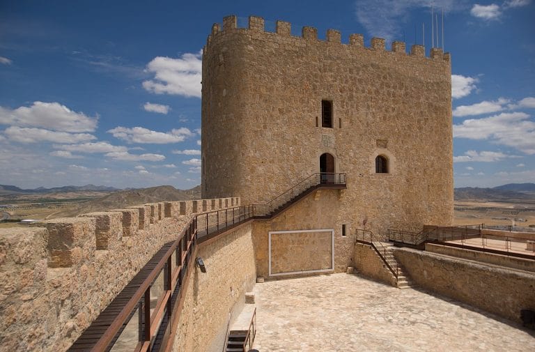 Vista interior de la torre del castillo de jumilla con pasarelas metálicas y murallas de piedra bajo un cielo con nubes.
