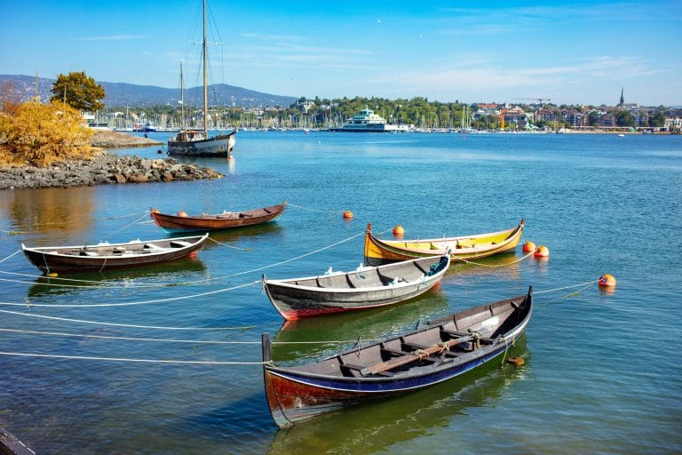 Barcas de madera amarradas en el puerto de Oslo, Noruega, con la ciudad y colinas al fondo