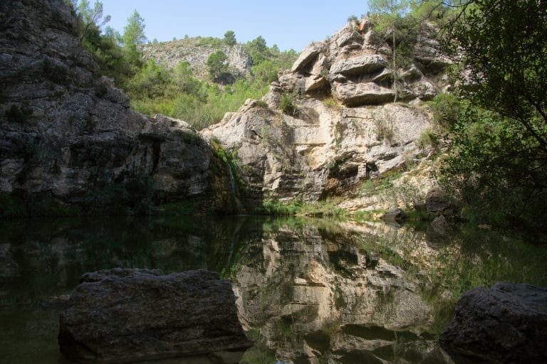 Vista del Barranco de la Encantada en Planes con una cascada y poza rodeada de rocas y vegetación