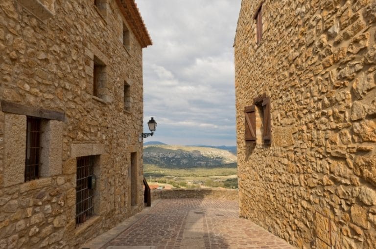 Calle empedrada en Culla con casas de piedra tradicionales y vistas a la montaña en el interior de Castellón
