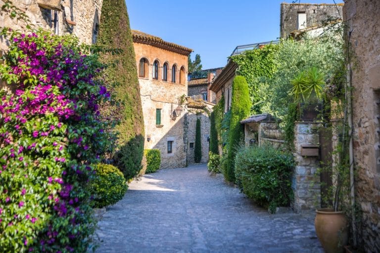 Calle empedrada de Peratallada con casas de piedra y flores en primavera