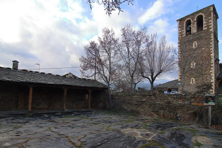 Plaza de la iglesia en Campillo de Ranas, Guadalajara, con suelos de pizarra, porche tradicional y torre campanario de arquitectura negra