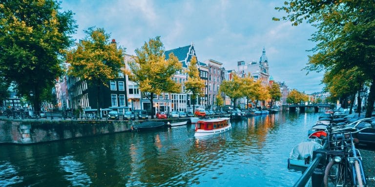 Vista de un canal en Ámsterdam con bicicletas, casas tradicionales y una barca en el agua al anochecer