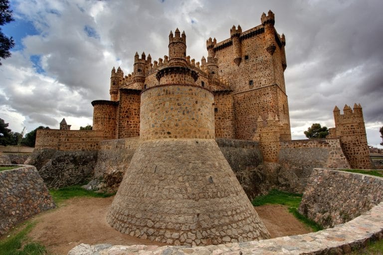 Vista del castillo de Guadamur en Toledo con su foso defensivo y torres almenadas bajo un cielo nublado