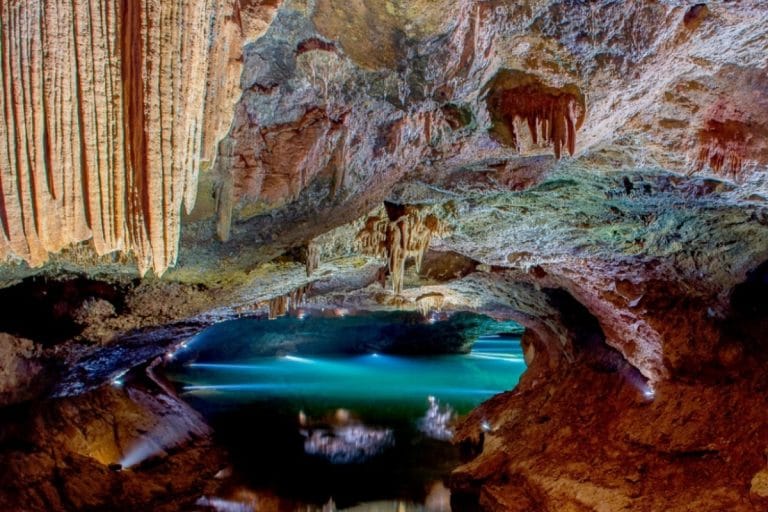 Interior de la Cova de Sant Josep en Castellón con estalactitas iluminadas y aguas turquesa del río subterráneo
