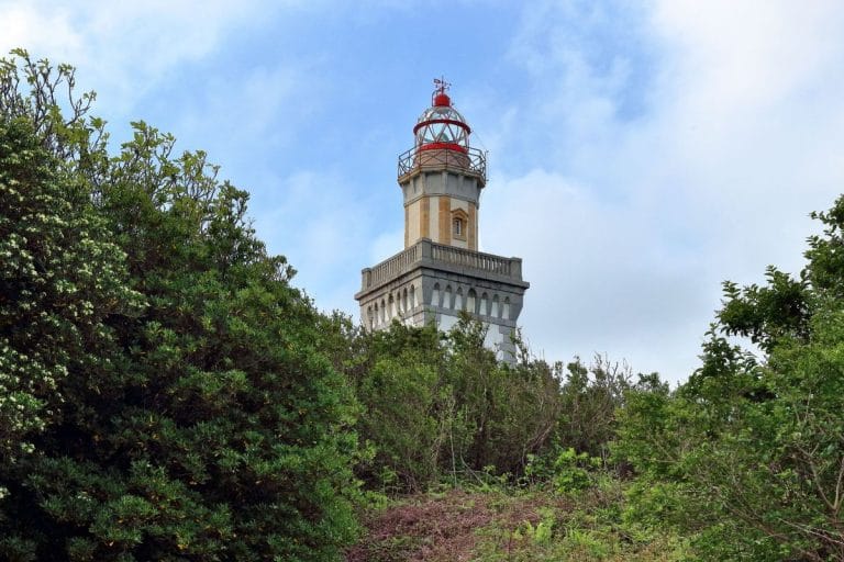 Faro de Higer en Hondarribia visto entre la vegetación, bajo un cielo parcialmente nublado.