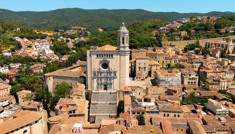 Vista aérea de la Catedral de Girona con su escalinata monumental, rodeada por el casco histórico y zonas verdes al fondo