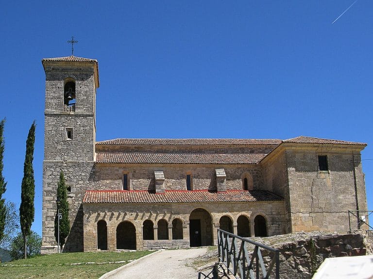 Fachada principal de la iglesia de la Asunción en Tamajón, Guadalajara, con pórtico románico y torre campanario bajo un cielo despejado