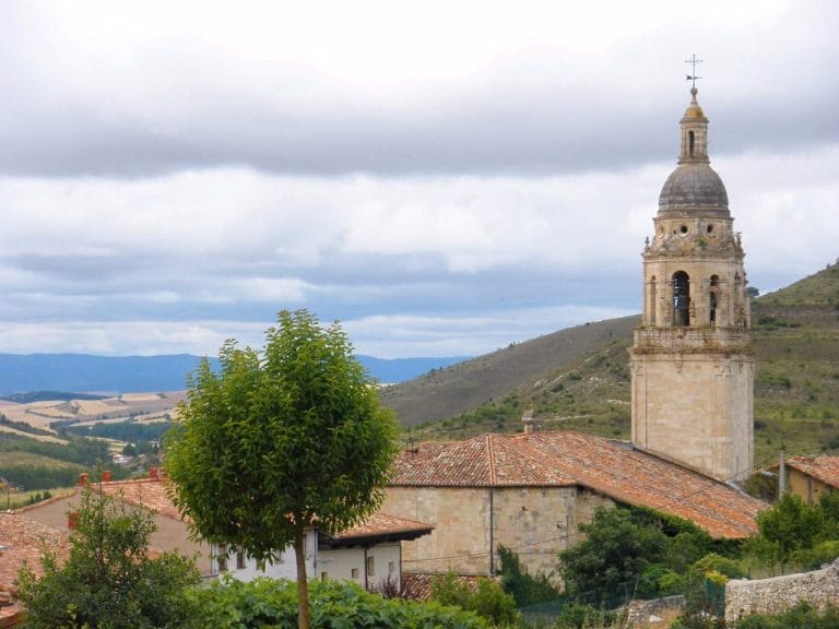 Torre de la iglesia de San Pedro Apóstol en Treviño, Burgos, con paisajes rurales al fondo.
