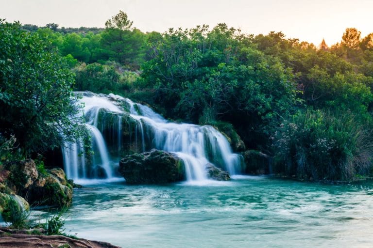 Cascada en las Lagunas de Ruidera al atardecer, rodeada de vegetación y agua cristalina