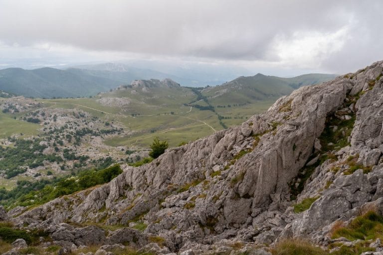 Vistas del Parque Natural de Aizkorri-Aratz con montañas rocosas, valles verdes y cielos nublados en el País Vasco.