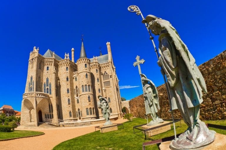Vista del Palacio Episcopal de Astorga, obra de Gaudí, con esculturas de peregrinos del Camino de Santiago en primer plano.