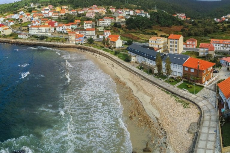 Vista aérea de la playa de Ézaro, con paseo marítimo y casas frente al mar en la Costa da Morte, Galicia.