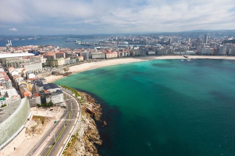 Vista aérea de la Playa del Orzán en A Coruña con aguas turquesas y ciudad al fondo, destino ideal en la costa gallega