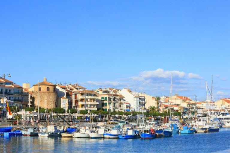 Puerto de Cambrils con barcos de pesca y edificios residenciales al fondo en un día soleado