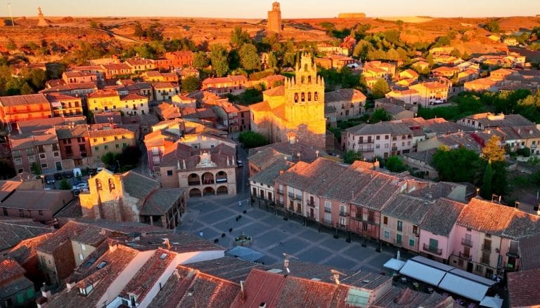 Vista aérea de la Plaza Mayor de Ayllón en Segovia al atardecer con la iglesia y casas tradicionales