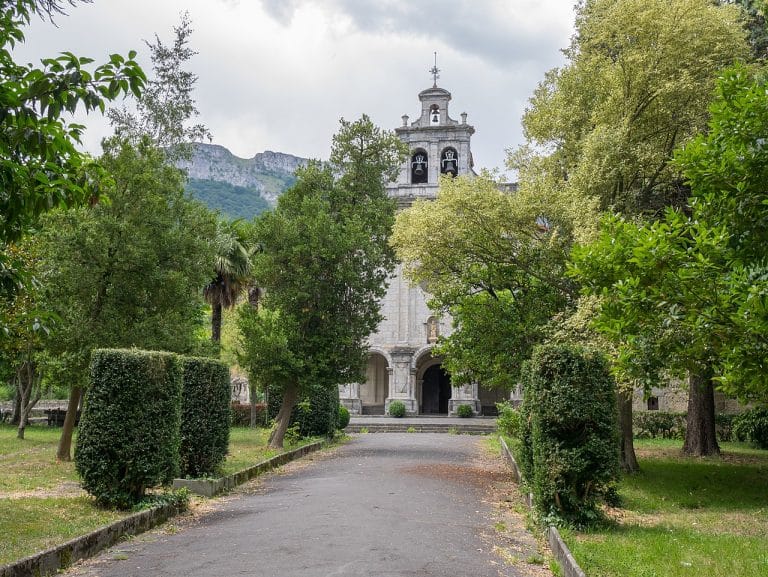 Santuario de Nuestra Señora de la Antigua en Orduña, rodeado de vegetación y montañas al fondo.