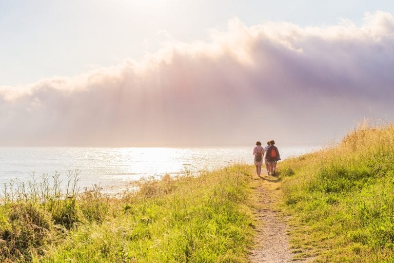 Pareja caminando por sendero costero junto al mar en Laxe, Galicia, al atardecer
