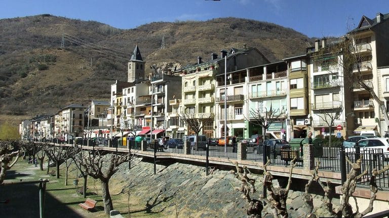 Vista del centro urbano de Sort, en Lleida, con fachadas de edificios, árboles podados y montañas al fondo