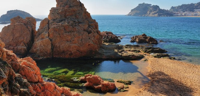 Formaciones rocosas y aguas cristalinas en una cala de Tossa de Mar, Costa Brava, con vistas al casco antiguo y al mar Mediterráneo.