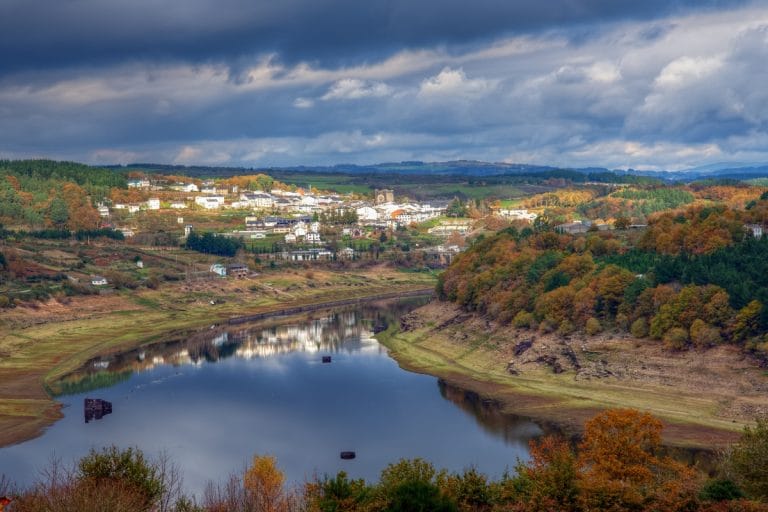 Vista panorámica de Portomarín con el embalse del río Miño en primer plano y el colorido paisaje otoñal al fondo.