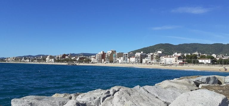Vista panorámica de Premià de Mar desde el mar, con edificios junto a la costa y montañas al fondo.