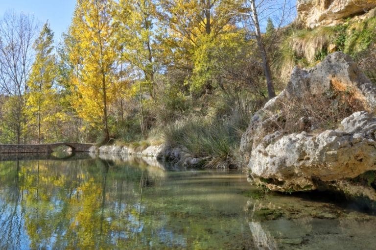 Paraje natural del Aguallueve de Anento, con puente de piedra y árboles reflejados en el agua cristalina