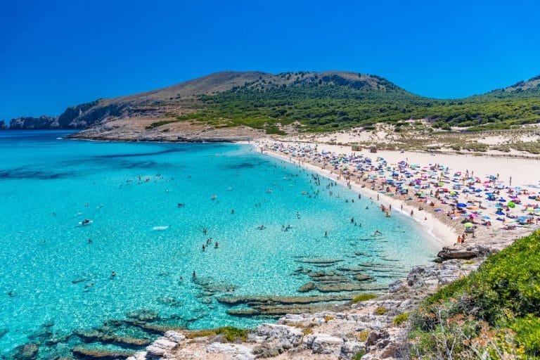 Playa de Cala Mesquida en Mallorca con aguas turquesas, arena blanca y bañistas disfrutando del verano