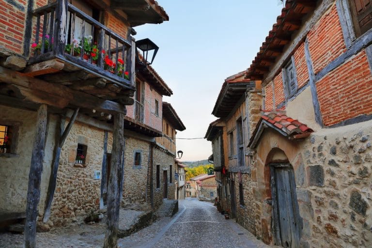 Vista de Calatañazor, un pintoresco pueblo medieval con un castillo y una torre en lo alto de una colina, con un campo verde brillante en el primer plano bajo un cielo azul y nublado