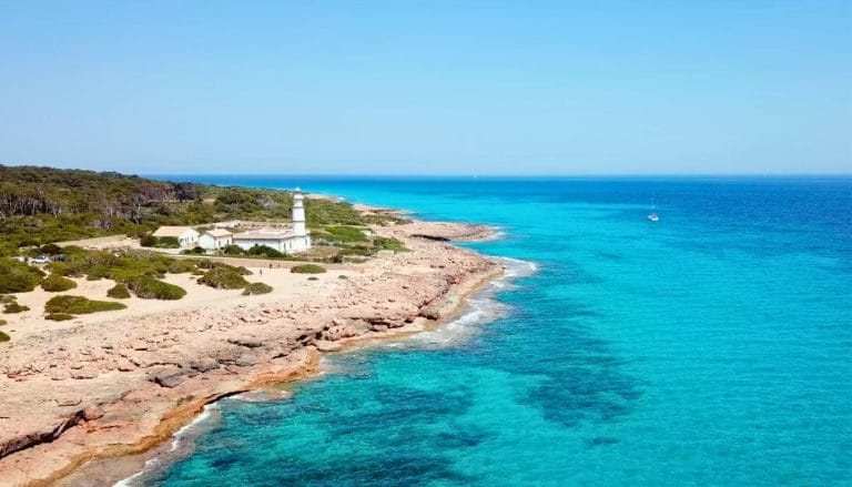 Faro de Ses Salines en Mallorca junto a la costa rocosa y aguas turquesas del Mediterráneo