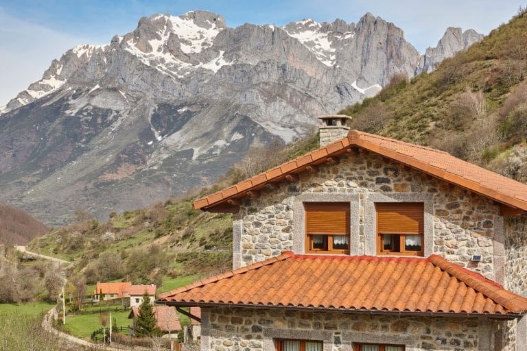 Casa de piedra típica en el Valle de Valdeón con las montañas nevadas de los Picos de Europa al fondo en León.