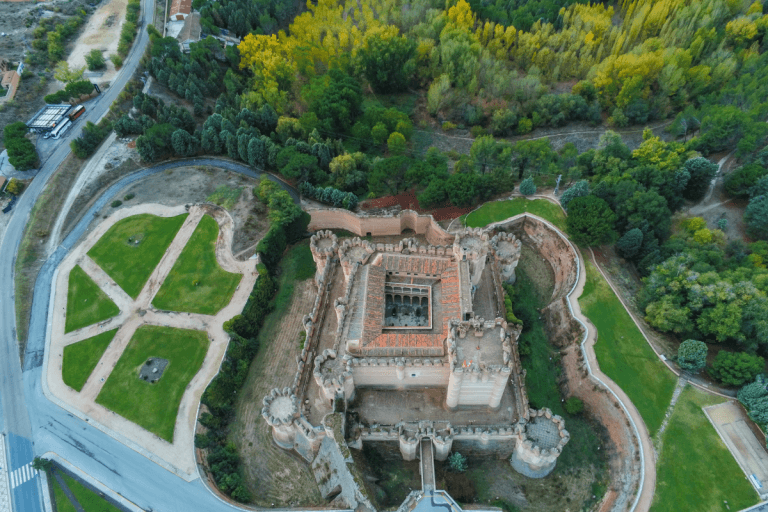 Vista exterior del Castillo de Coca, mostrando la elaborada arquitectura mudéjar de ladrillo con numerosas torres y un foso seco en la parte inferior, bajo un cielo nublado