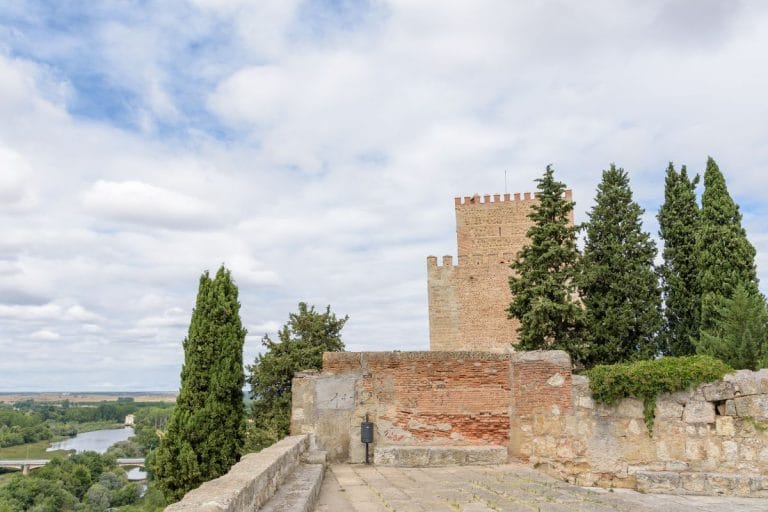 Vista de un castillo de piedra con una torre y árboles altos, con vistas al río Águeda y al campo de Ciudad Rodrigo en Salamanca.