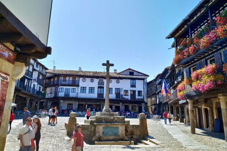 Plaza Mayor de La Alberca en Salamanca con casas tradicionales de entramado de madera, balcones con flores y cruz de piedra en el centro de la plaza