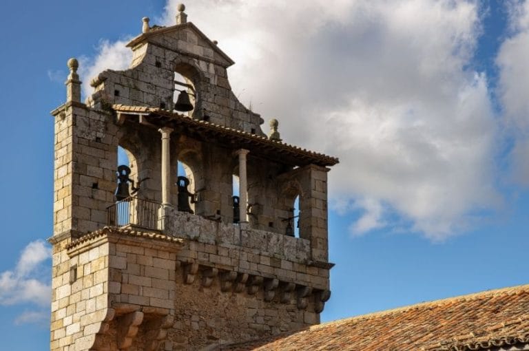 Vista de la torre del campanario de la iglesia de San Martín del Castañar, de piedra y estilo renacentista, con varias campanas y una balconada.